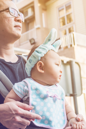 baby girl in a baby carrier with father, outdoors portraitの写真素材