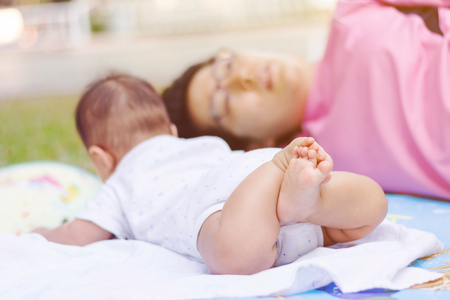 cute Asian baby laying down on ground at park with motherの写真素材