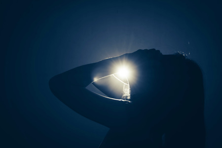 silhouette of depress woman standing in the dark with light shine behindの写真素材