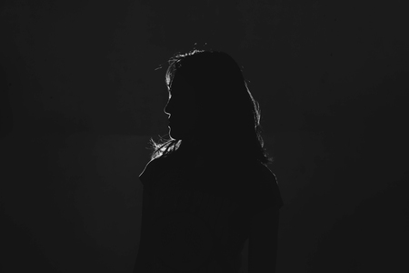 silhouette of depress woman standing in the dark with light shine behind, white toneの写真素材