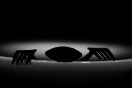 spoon and fork on empty plate in white tone, diet, poverty or afraid of eating concept の写真素材