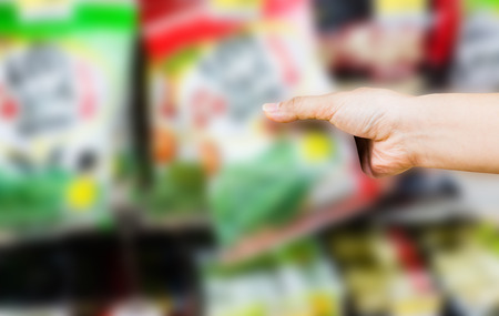 hand of woman choosing or taking sweet products, snacks on shelves in convenience storeの写真素材