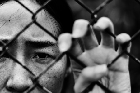 Depressed woman standing behind a fence, hand grabs steel mesh cage,close up on face in white tone, abuse conceptの写真素材