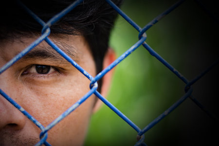 Depressed man standing behind a fence ,close up on face , abuse concept