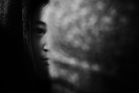 fear girl hiding behind curtain in white tone with shadow edgeの写真素材