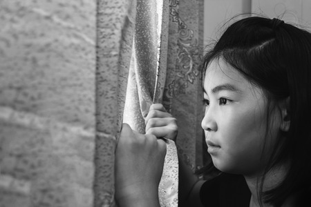 girl open curtain looking outside with absent minded, hopeful conceptの写真素材