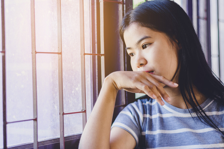 Portrait  beautiful Asian woman, depress and looking out the window at sunset  の写真素材