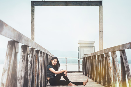 portrait of young woman sitting at walk way to water level gateの写真素材