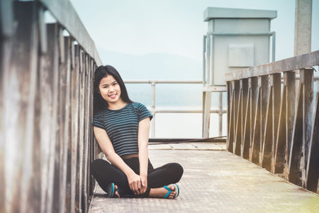 portrait of young woman sitting at walk way to water level gateの写真素材