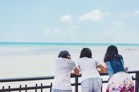 Sweet Asian girls standing behind fence and enjoy fresh air of seaの写真素材