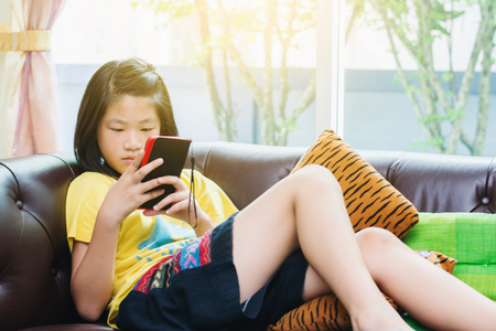Sweet Asian Girl playing game in mobile phone at homeの写真素材