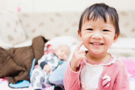 Closeup of happy little child playing over the bed in a relaxed morning with her little baby sister.の写真素材
