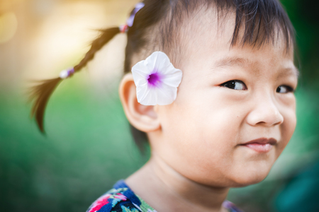 Portrait of Sweet Asian child little girl smiling with flower on her earの写真素材