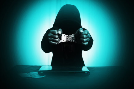 Boy in hood with handcuff at desk with laptop and money ,Cyber Crime concept