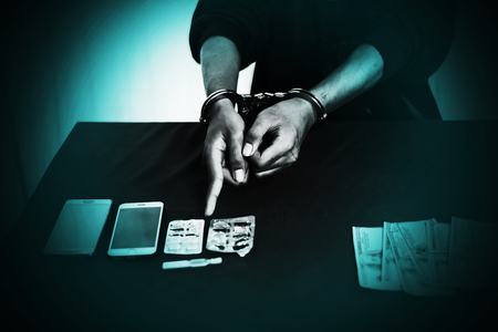 Boy in hood with handcuff at desk with money and Drug ,Crime and Drug conceptの写真素材