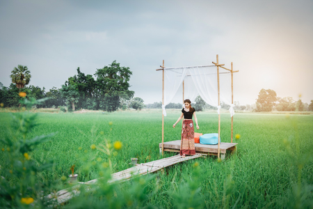 Beautiful Asian woman in local dress standing in small bamboo pavilion with cloth decoration and enjoy natural on bamboo bridge in rice fieldの写真素材