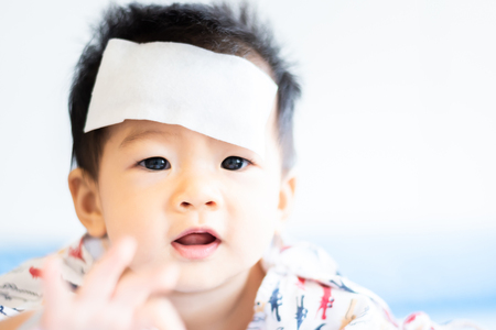 Unhappy Asian little baby child sick with cool fever jel pad on foreheadの写真素材