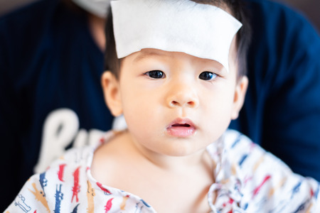 Unhappy Asian little baby child sick with cool fever jel pad on foreheadの写真素材