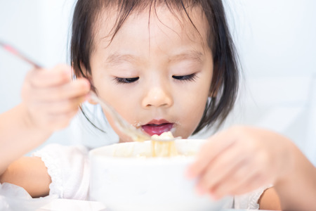 Asian little baby child eating noodle and enjoy breakfast by herselfの写真素材