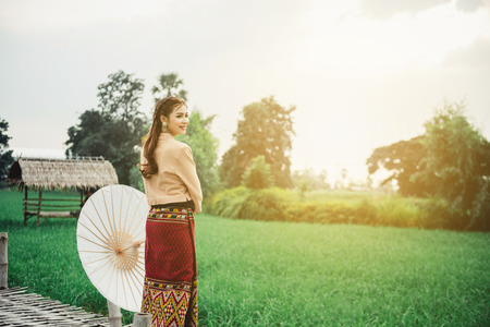 Beautiful Asian woman in local dress holding paper umbrella standing and enjoy natural on bamboo bridge in rice fieldの写真素材