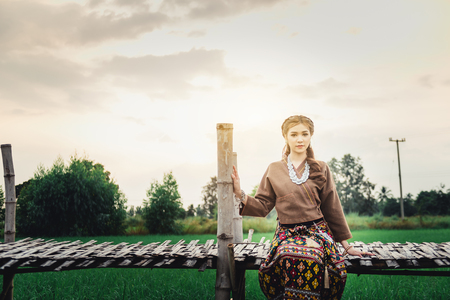 Beautiful Asian woman in local dress sitting and enjoy natural on bamboo bridge in rice fieldの写真素材