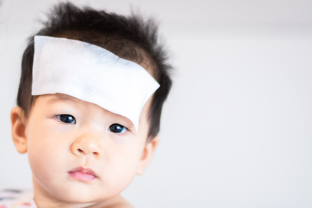 Unhappy Asian little baby child sick with cool fever jel pad on foreheadの写真素材