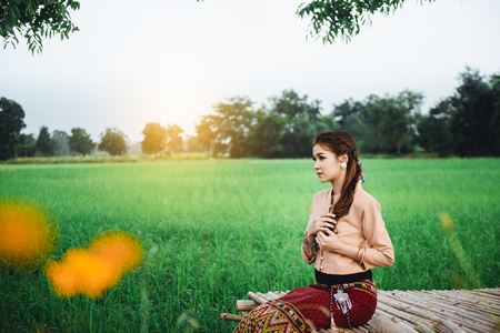 Beautiful Asian woman in local dress sitting and enjoy natural on bamboo bridge in rice fieldの写真素材