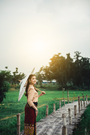 Beautiful Asian woman in local dress holding paper umbrella standing and enjoy natural on bamboo bridge in rice fieldの写真素材