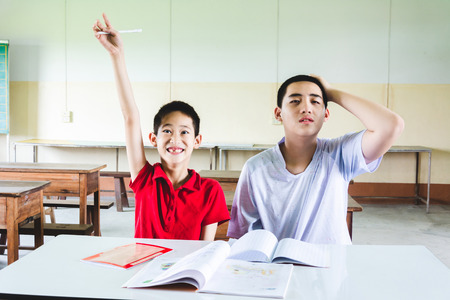 Boy confused with answer but another on hand raise up to answer the questionの写真素材