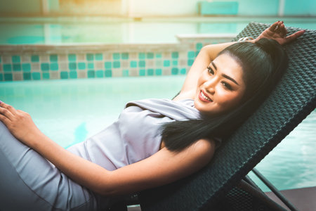 Beautiful Asian woman relaxing on folder chiar and enjoy fresh air beside swimming pool