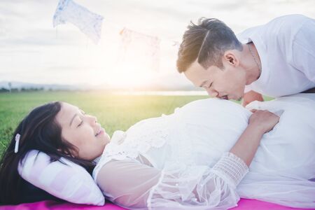 Asian husband kissing his pregnant wife with his eyes closed. Asian Married couple and family concept.の写真素材