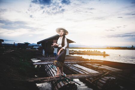 Asian Beautiful woman in Thai local dress standing on boat in fishing village with field and lake backgroundの写真素材