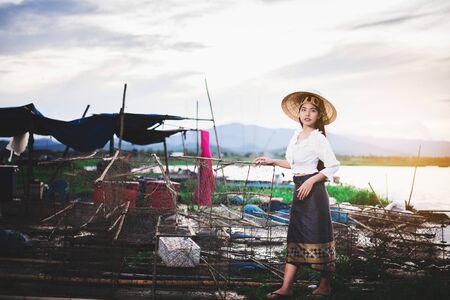 Portrait of Asian Beautiful woman in Thai local dress working with fishing net in fishing village with field and lake backgroundの写真素材