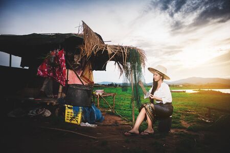 Portrait of Asian Beautiful woman in Thai local dress sitting and working with fishing net in fishing village with field and lake backgroundの写真素材