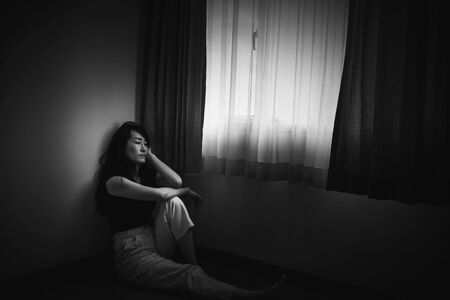 depress woman sitting on floor in room near window in white tone, sadness and depress conceptの写真素材