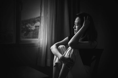 depress woman sitting on chair in room near window in white tone, sadness and depress conceptの写真素材