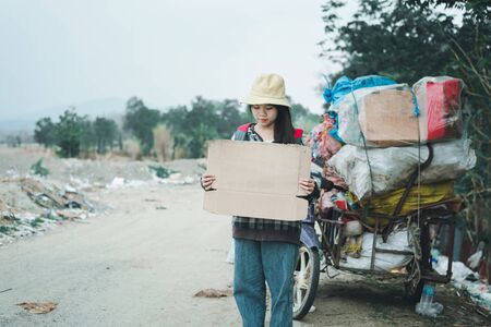 Homeless woman holding sign with hat and backpack standing on a road の写真素材