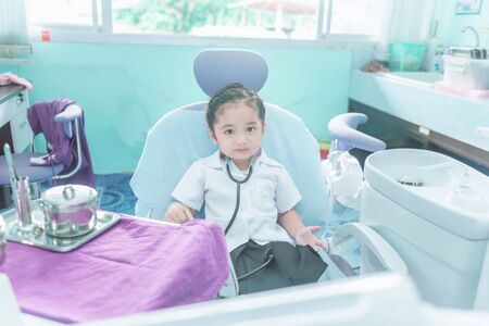 A Cute and lovely Asian baby girl in nurse uniform dress sitting on dental chairの写真素材