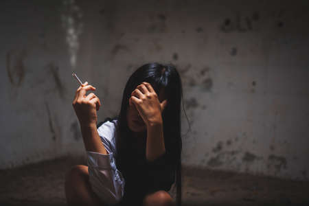 photo of children hand on forehead with lower head with cigarette in her hand at dark corner, imprison, retarded, Child Abuseの写真素材