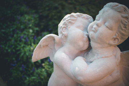 Cute little angels sculptures kissing in the garden. Concept of love.の写真素材