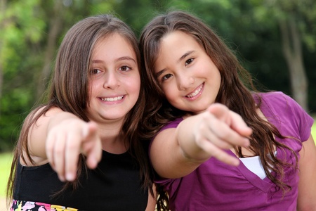 Two young girls smiling and pointing the camera, outdoor imageの写真素材