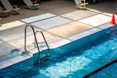 Part of the pool with a ladder to enter the water, white sun loungers in the background
