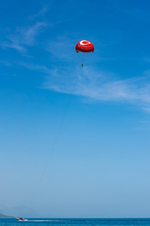 A man is parasailing. The boat is towing a red parachute against a blue sky.の写真素材