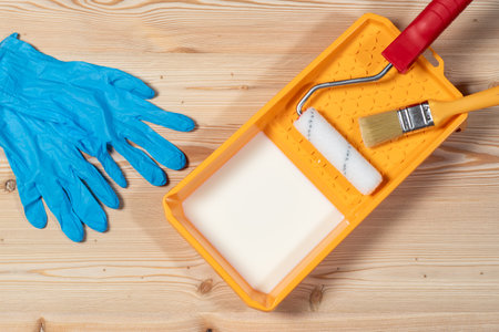 Tray with white liquid wax-oil for wood, brush, roller and gloves on a wooden background, before paintingの写真素材