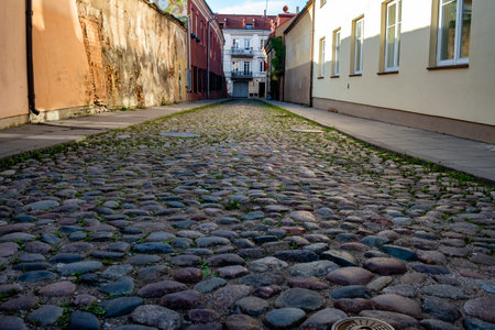 A narrow cobbled street in Vilnius with old brick and plaster walls. Evening light casts soft...