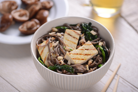 Portion of Soba noodles with grilled tofu, peanuts and spinach. Shiitake mushrooms addition and green tea. Meal in Oriental style.の写真素材