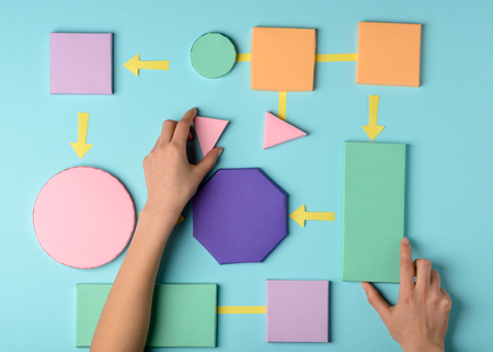 Hands laying paper figures out on blue background. Colorful concept of planning process, algorithm.の写真素材