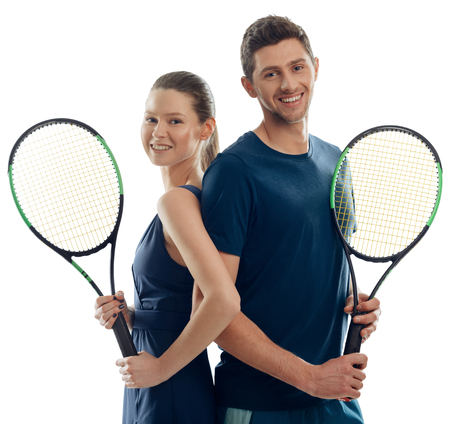Couple of adult tennis players. Athletic woman and man giving cheerful smiles, holding racquets and wearing uniforms.の写真素材