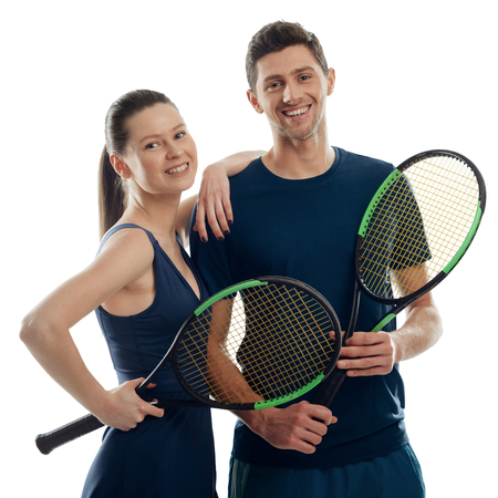 Couple of young tennis players on white. Woman leant on mans shoulder, both holding racquets and giving friendly smiles.の写真素材