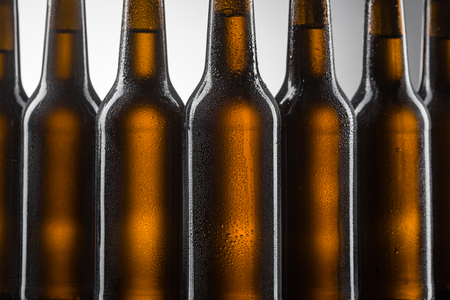 Bottles of beer in line on light grey background. Brown color of glass covered with tiny water drops. Cool low alcohol beverage.の写真素材